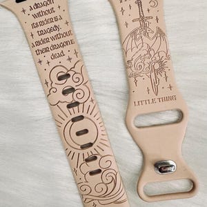 May include: Two beige leather Apple Watch bands with engraved designs. One band features a sun, moon, and clouds with the text "a dragon without its rider is a tragedy. a rider without their dragon is dead." The other band features a dragon, sword, and clouds with the text "VIOLENT LITTLE THING".