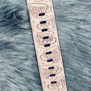 May include: A light beige silicone watch band featuring a laser-engraved pattern of a teapot filled with flowers at the top, followed by a series of six distinct teacups arranged vertically along the length of the strap, interspersed with small star icons.