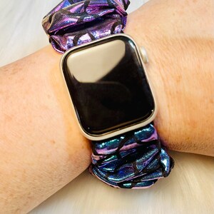 May include: A purple and blue iridescent watch band with a black pattern. The band is made of a soft, stretchy material and is designed to fit a smartwatch.