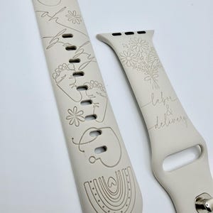 May include: A light beige silicone watch band featuring laser-engraved designs including a fetus, baby footprints, a rainbow, and flowers. The text "oh baby" is engraved on the longer strap, while "labor & delivery" appears on the shorter strap.