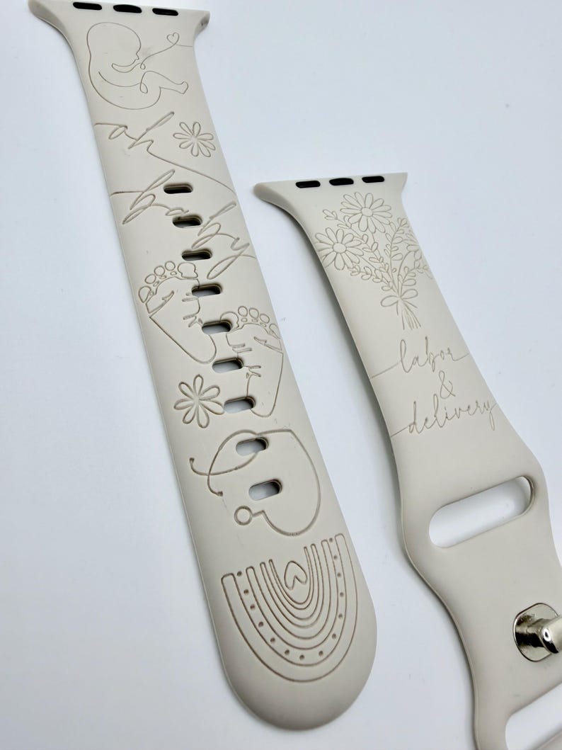 May include: A light beige silicone watch band featuring laser-engraved designs including a fetus, baby footprints, a rainbow, and flowers. The text "oh baby" is engraved on the longer strap, while "labor & delivery" appears on the shorter strap.