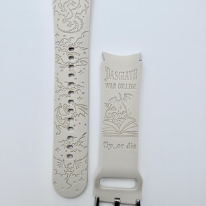 May include: A light beige silicone watch band featuring laser-engraved dragon illustrations and clouds. One strap displays the text Basgiath War College above an open book graphic and the phrase fly...or die, while the other shows multiple dragons.