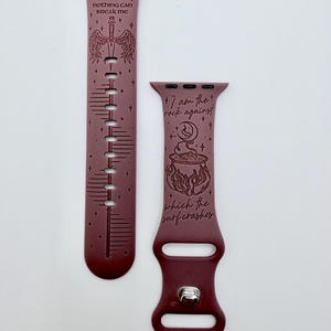 May include: A dark maroon silicone watch band featuring engraved designs. One strap displays a sword with wings and the text VALKYRIE nothing can BREAK ME. The other strap shows a cauldron, a moon, and the text I am the rock against which the surf crashes.