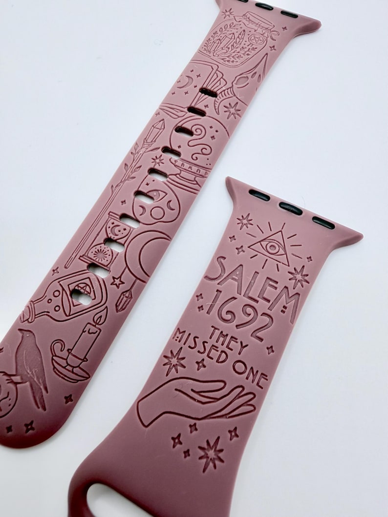 May include: A dusty rose silicone watch band featuring engraved occult-themed illustrations including a crystal ball, hourglass, raven, and candle. The text reads SALEM 1692 THEY MISSED ONE, accompanied by an all-seeing eye symbol and a hand graphic.