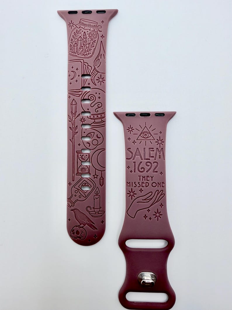 May include: A mauve silicone watch band featuring engraved occult-themed illustrations including a raven, skull, hourglass, and crystals. The text SALEM 1692 THEY MISSED ONE is engraved on the shorter strap along with an eye symbol and a hand.