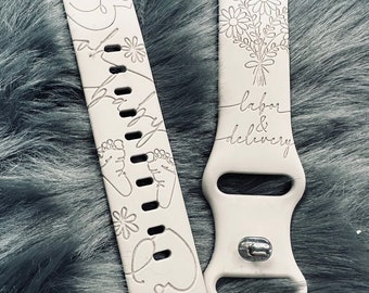 Puede incluir: Dos bandas blancas para Apple Watch con diseños grabados. Una banda presenta un contorno de bebé, huellas de pies y la palabra "bebé". La otra banda tiene un diseño floral y las palabras "trabajo de parto y parto".