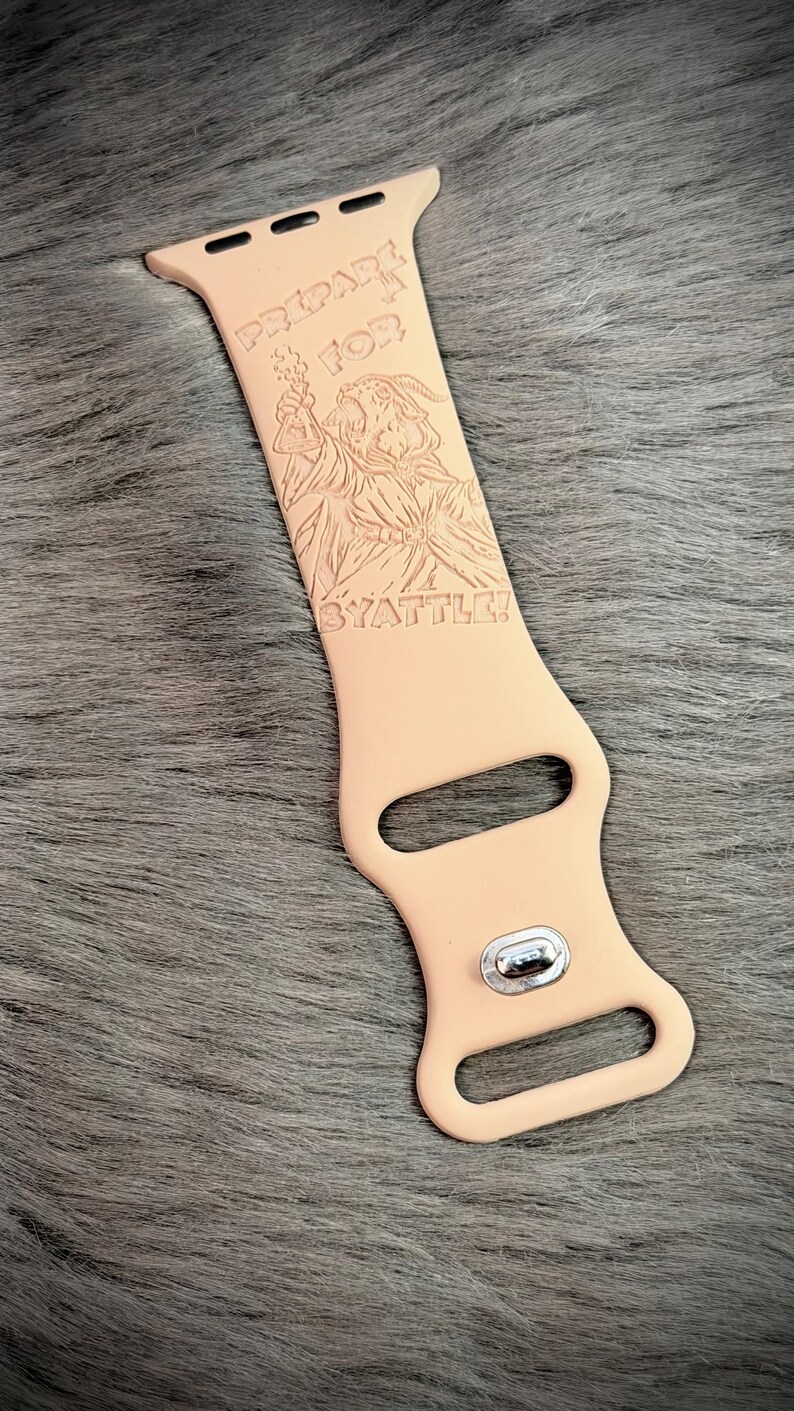 May include: A light peach-colored silicone watch band featuring an engraved illustration of a wizard holding a potion bottle. The text "PREPARE FOR BYATTLE!" is etched above and below the wizard figure. The band includes a silver metal pin.
