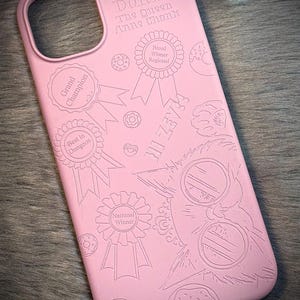 May include: Pink phone case with engraved text and illustrations. The case features the words "Princess Donut The Queen Anne Chonk" and various award ribbons. Donuts are also illustrated on the case.
