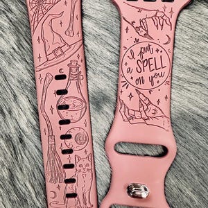 May include: Two pink watch straps with etched Halloween designs. One strap features a witch's hat, broom, potion bottle, cat, and cauldron. The other has the text "I put a SPELL on you" and a hand with long nails.