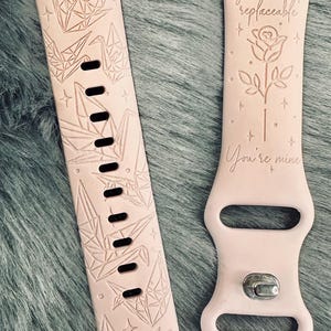 May include: Two pink silicone Apple Watch bands with different designs. The band on the left has a pattern of origami cranes and stars. The band on the right has a rose and the text "You are not replaceable. You're mine."