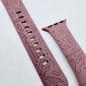 May include: A mauve silicone watch band featuring embossed occult-themed illustrations including a jar, crystals, moon phases, a skull, a raven, and a candle. The text "SALEM 1692 THEY MISSED ONE" is engraved on the shorter strap alongside an eye symbol.