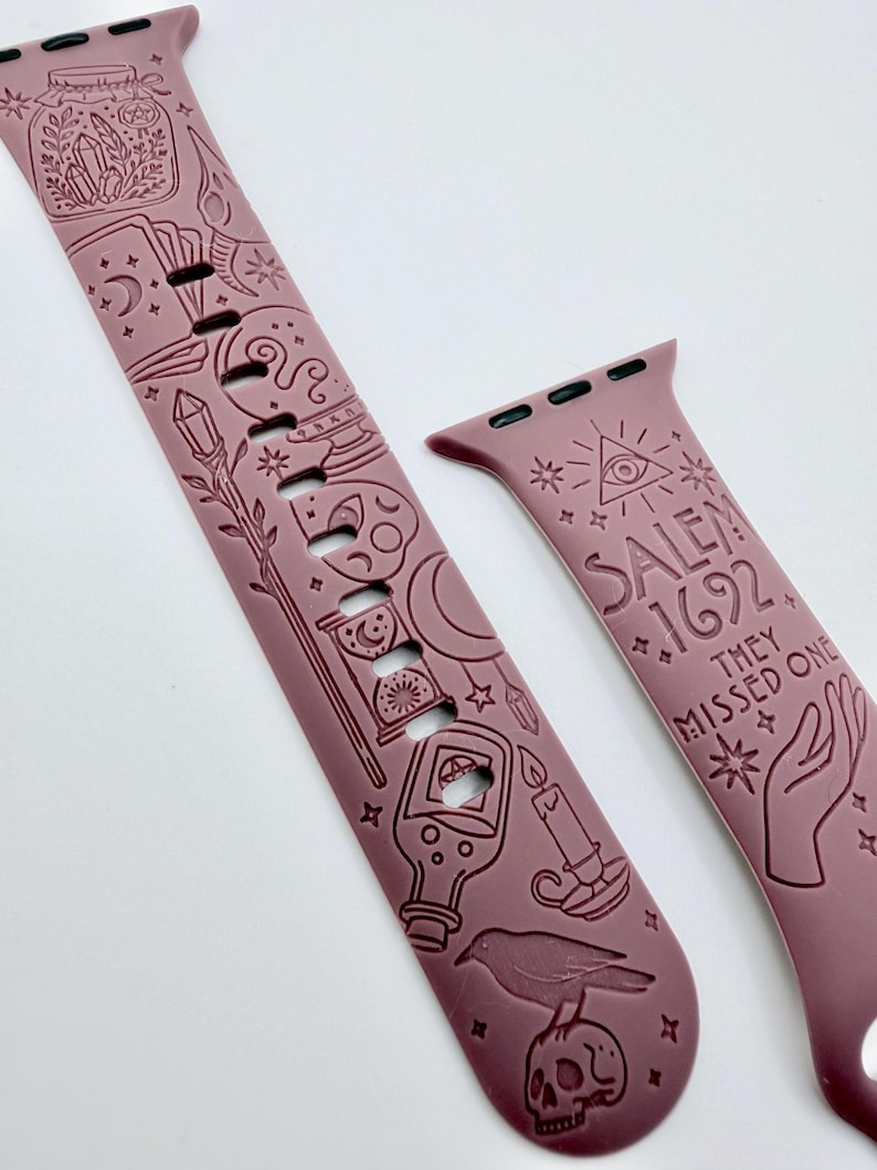 May include: A mauve silicone watch band featuring embossed occult-themed illustrations including a jar, crystals, moon phases, a skull, a raven, and a candle. The text "SALEM 1692 THEY MISSED ONE" is engraved on the shorter strap alongside an eye symbol.