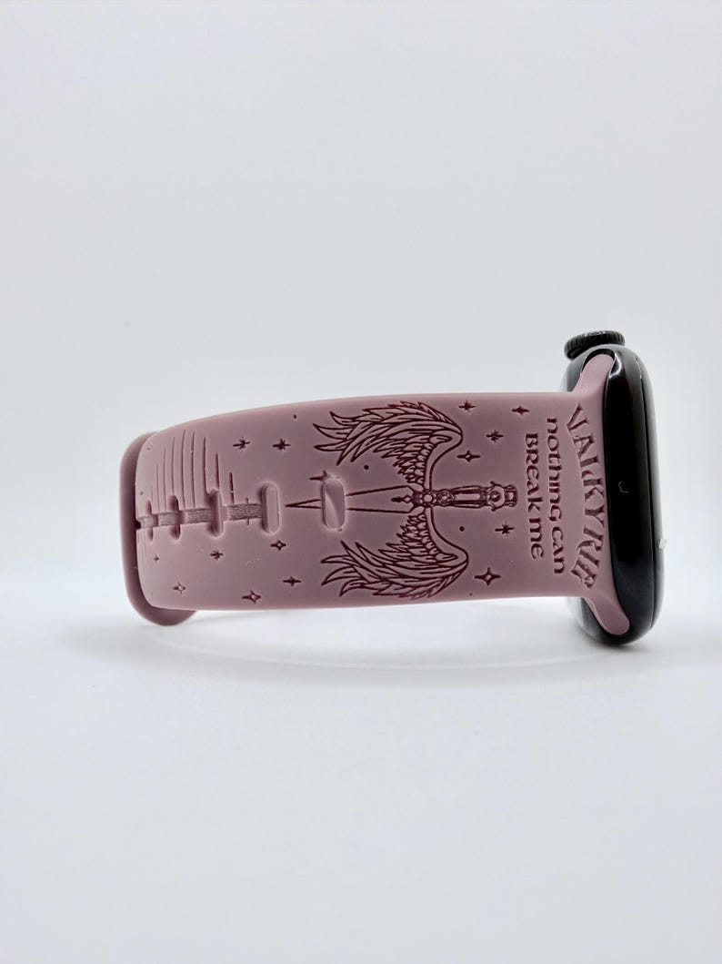 May include: A dusty rose silicone watch band featuring a dark engraved design of a sword with wings, small stars, and the text VALKYRIE nothing can BREAK me. The band is attached to a black smartwatch case with a side dial visible on the right.