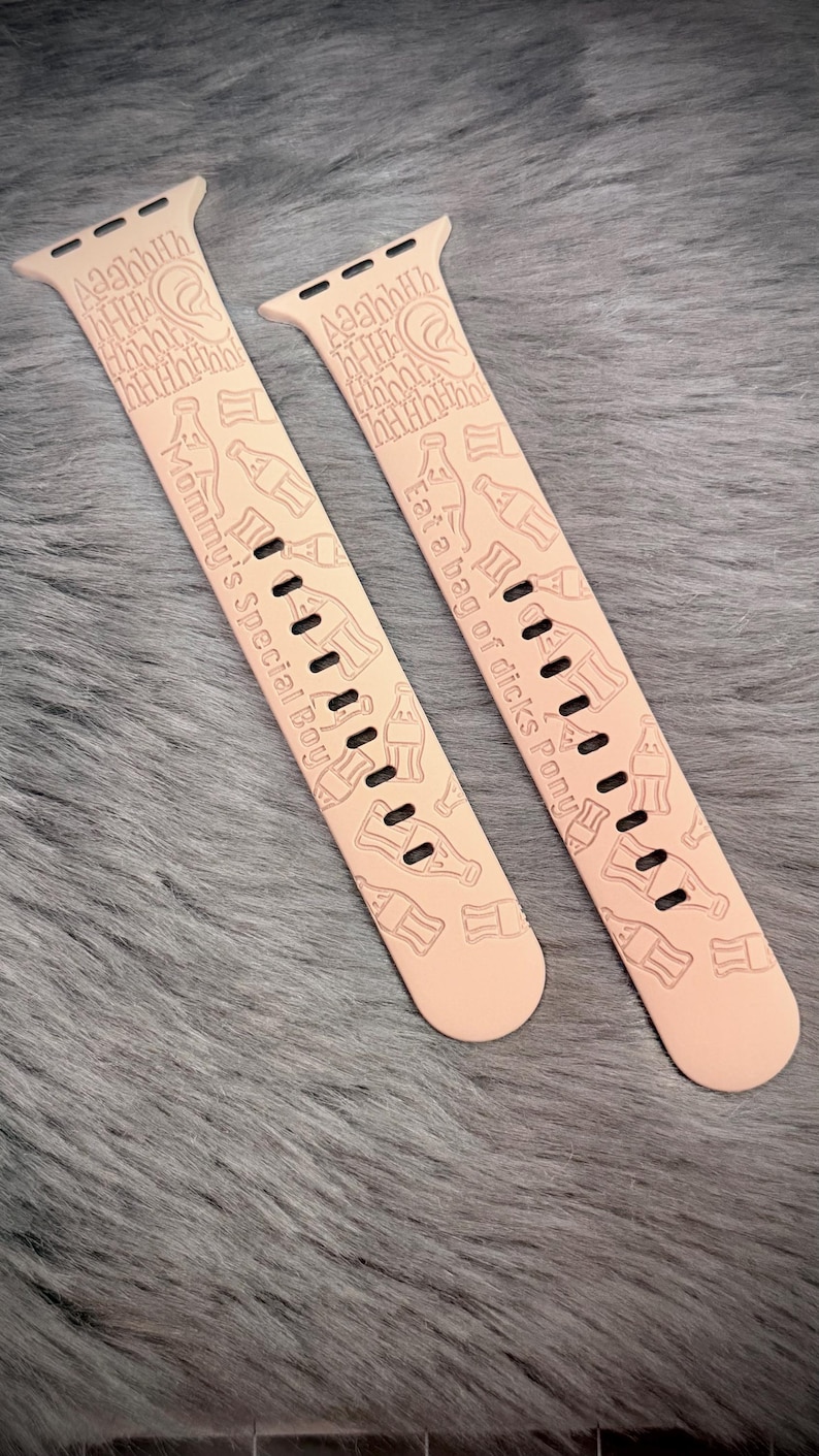May include: A pair of light peach silicone watch bands featuring engraved patterns of soda bottles, an ear icon, the text Aaahhh, and the phrases Mommy's Special Boy and Eat a bag of dicks Pony, with standard attachment hardware at the top ends.