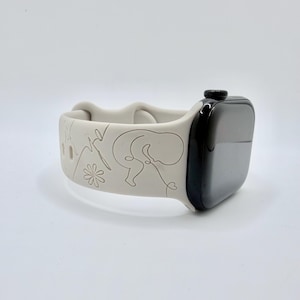 May include: A light gray silicone watch band attached to a black smartwatch. The band features a continuous line drawing design depicting a fetus, a flower, and a heartbeat rhythm line engraved into the surface of the flexible material.