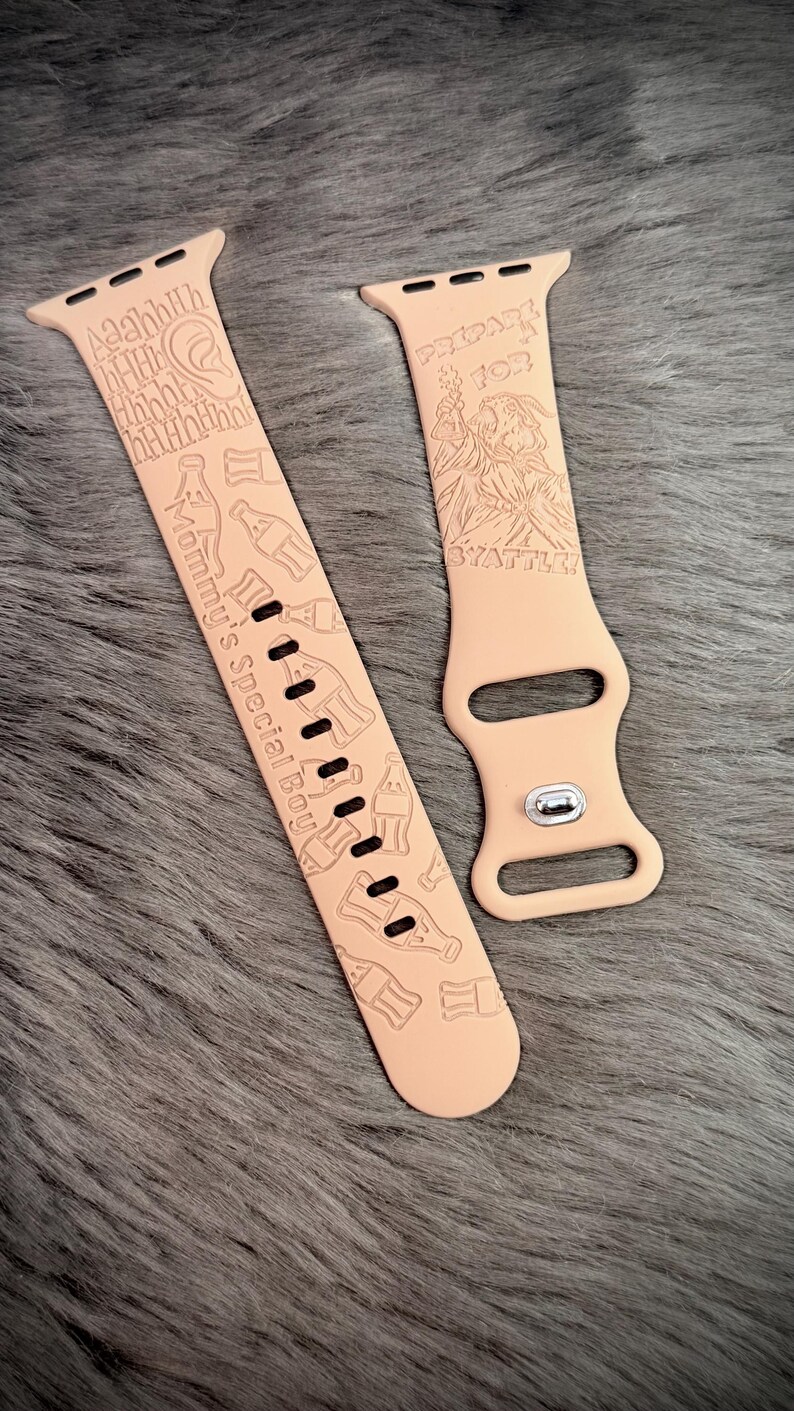 May include: A light peach-colored silicone watch band featuring engraved graphics of soda bottles, a character, and text that reads "Aaahhh", "Mommy's Special Boy", "PREPARE FOR BYATTLE!" with a silver metal pin closure on the shorter strap section.