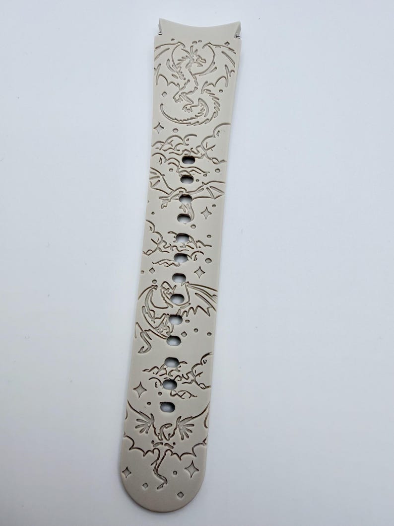 May include: A light beige silicone watch band featuring an engraved pattern of multiple dragons flying among clouds and stars. The strap includes a series of vertical adjustment holes running down the center, with a curved connector end piece.