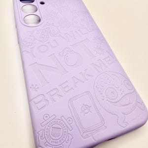 May include: A light purple smartphone case featuring embossed graphic designs including a skull, a bomb, a United States Coast Guard emblem, and a creature. The text "YOU WILL NOT BREAK ME!" is prominently displayed across the center surface.