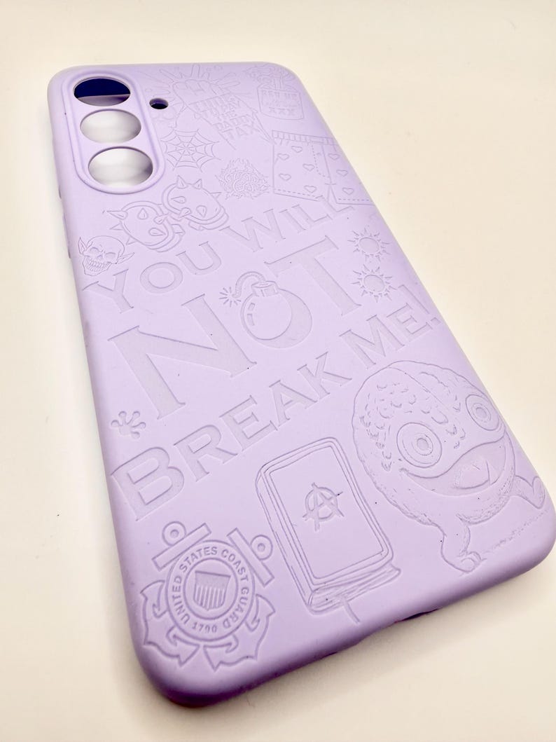 May include: A light purple smartphone case featuring embossed graphic designs including a skull, a bomb, a United States Coast Guard emblem, and a creature. The text "YOU WILL NOT BREAK ME!" is prominently displayed across the center surface.