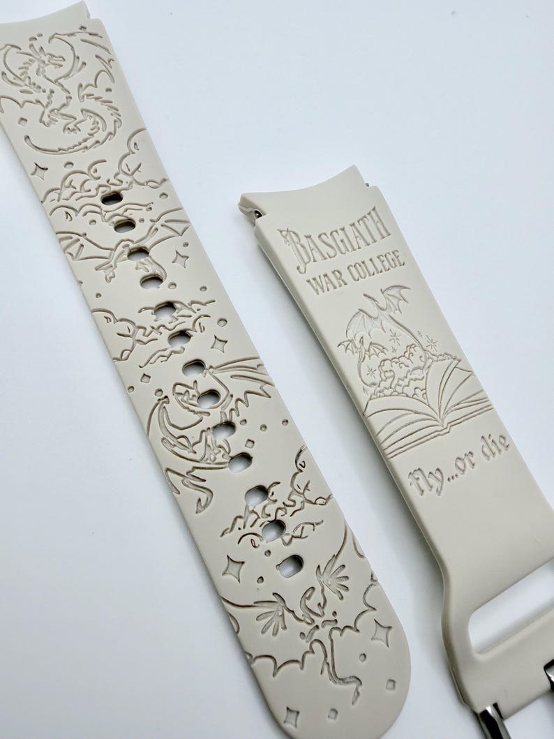 May include: A light beige silicone watch band featuring engraved dragon motifs, stars, and clouds. One section displays the text "BASGIATH WAR COLLEGE" above an open book illustration and the phrase "fly...or die" in a stylized serif font.