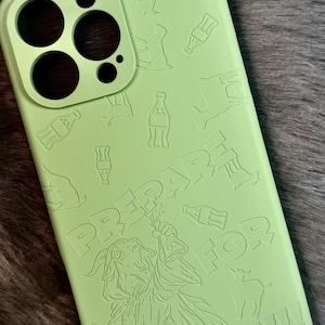 May include: A light green phone case with a design that includes the words "PREPARE FOR BYATTLE!!!" and illustrations of a goat-like figure, bottles, and animals. The case has cutouts for the phone's camera and buttons.