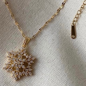 Könnte beinhalten: Eine goldene Kettenkette mit einem Schneeflockenanhänger aus kleinen klaren Kristallen.