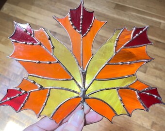 May include: A stained glass maple leaf with red, orange, and yellow glass pieces. The leaf is outlined in copper and has small copper beads along the edges.