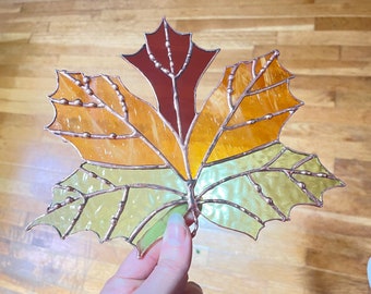 May include: A stained glass autumn leaf with copper accents. The leaf is made of three different colors of glass: red, orange, and yellow. The leaf is a popular decoration for the fall season.