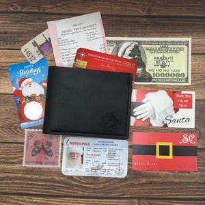 May include: A black leather wallet with a Santa Claus logo. The wallet is open and contains a North Pole Bank and Trust Gold credit card, a North Pole International Sleigh Drivers License for Santa Claus, a $1,000,000 bill, and a Christmas card.