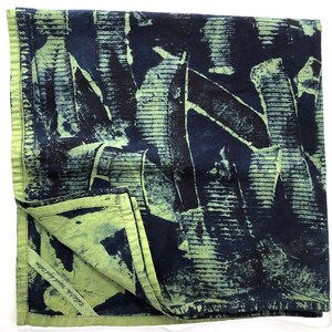 Peut inclure: Un textile carré en coton plié avec un motif abstrait bleu foncé et vert. Le motif présente des lignes et des formes verticales et horizontales. Les bords sont vert clair, et le coin est replié, révélant le texte "Scottish Hand Dyed Cotton."