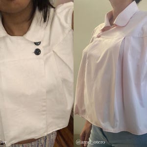 May include: Two short-sleeved blouses in the image. One is white with black buttons, and the other is light pink with a single button. Both have a collared neckline and pleated front details. The blouses are made of a smooth fabric.