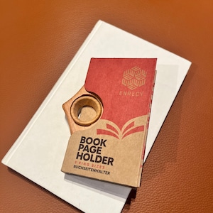 May include: A wooden book page holder with a red and white box that says "Book Page Holder 3 Ring Sizes Buchseitenhalter" and "Enrecy" on the front.
