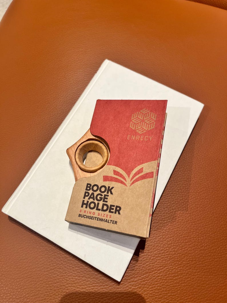 May include: A wooden book page holder with a red and white box that says "Book Page Holder 3 Ring Sizes Buchseitenhalter" and "Enrecy" on the front.