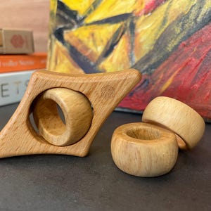 Könnte beinhalten: Holzspielzeug-Set mit einem sternförmigen Ring und zwei runden Ringen. Die Ringe sind aus Naturholz gefertigt und haben eine glatte Oberfläche.