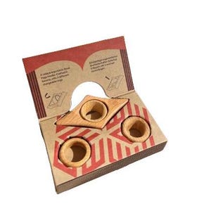 May include: A set of three wooden ring holders in the shape of a triangle. The holders are made of natural wood and have a light brown color. The holders are packaged in a cardboard box with a red and white geometric pattern.