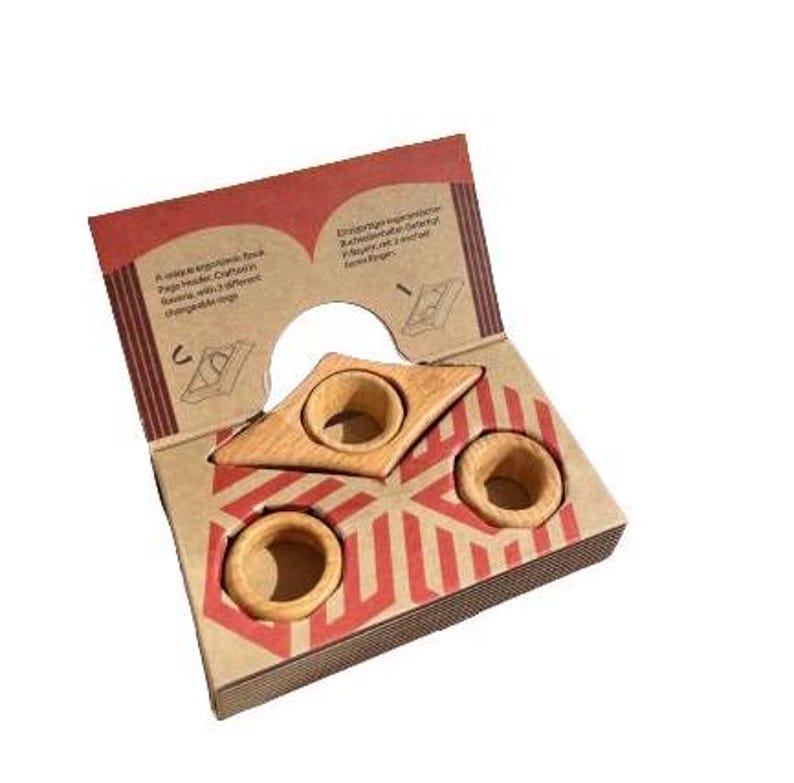 May include: A set of three wooden ring holders in the shape of a triangle. The holders are made of natural wood and have a light brown color. The holders are packaged in a cardboard box with a red and white geometric pattern.