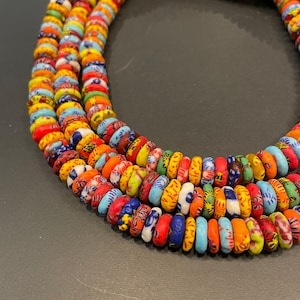 Puede incluir: Un collar de múltiples hilos hecho de cuentas de vidrio coloridas y estampadas. Las cuentas son pequeñas y redondas, y están dispuestas en un patrón aleatorio. El collar es una pieza de joyería vibrante y llamativa.
