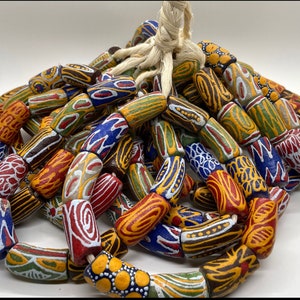 May include: A collection of colourful, hand-painted, cylindrical beads with intricate patterns. The beads are made of clay and have a variety of colours, including red, blue, green, yellow, and white. The beads are strung together on a white cord.
