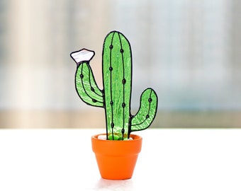May include: A green stained glass cactus with a white flower in a small orange pot.