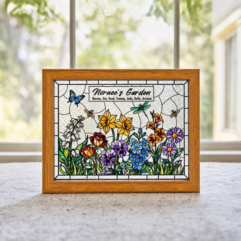May include: A rectangular stained glass panel in a light wood frame featuring a garden scene with yellow daffodils, red roses, purple pansies, blue forget-me-nots, and orange flowers. A blue butterfly, a dragonfly, and two bees are present. Text reads: Nornee's Garden, Norma, Jim, Brad, Tommy, Jade, Bella, Arriana.