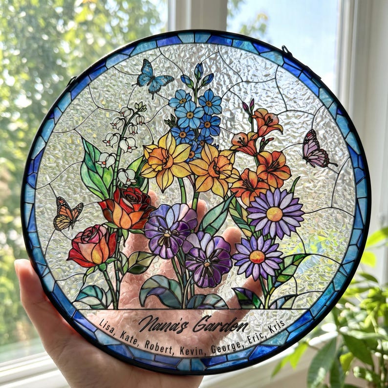 May include: A circular stained glass suncatcher featuring a colorful floral arrangement with roses, daffodils, and daisies, accented by three butterflies. The bottom border includes the text "Nana's Garden" followed by the names Lisa, Kate, Robert, Kevin, George, Eric, and Kris.
