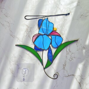 May include: A stained glass window hanging with a blue, pink, and yellow iris flower design.