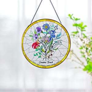 May include: Round stained glass window with a floral bouquet design. The bouquet includes red, purple, blue, and white flowers. The words "Grandmas Brunch" are written across the bottom, along with names. A gold border surrounds the glass.