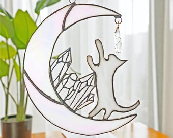 May include: A stained glass moon with a white cat reaching up to a crystal hanging from the crescent moon. The cat is standing on a bed of crystals.