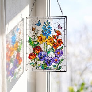 May include: A rectangular stained glass panel depicting a colourful floral design with roses, pansies, and other flowers in red, orange, yellow, blue, and purple. Butterflies are also shown. The panel is framed in black and suspended by a chain.