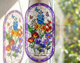 May include: An oval stained glass suncatcher featuring a vibrant floral arrangement with blue, yellow, orange, red, and purple flowers, green leaves, and butterflies. The text Nana's Garden and several names are printed at the bottom of the piece.