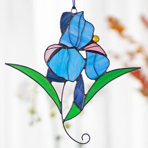 May include: A stained glass iris flower with blue, pink, and green glass pieces. The flower is hanging from a black wire.