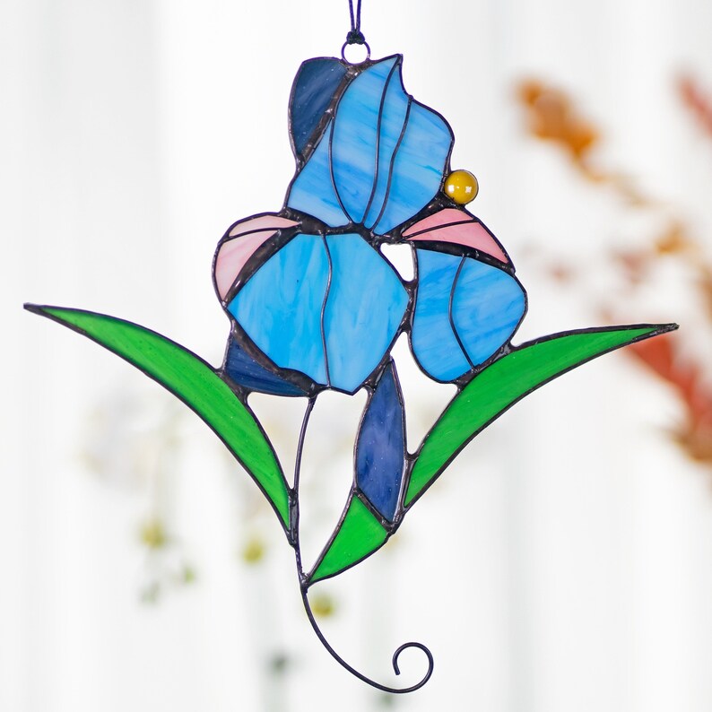 May include: A stained glass iris flower with blue, pink, and green glass pieces. The flower is hanging from a black wire.