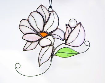 May include: A stained glass hanging ornament featuring a white magnolia flower with a pink center and a green leaf. The flower is attached to a black string.
