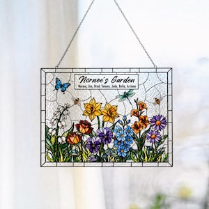 May include: A rectangular stained glass suncatcher featuring a garden scene with colorful flowers, a blue butterfly, a dragonfly, and bees. The text reads Nornee's Garden followed by the names Norma, Jim, Brad, Tommy, Jade, Bella, and Arriana.